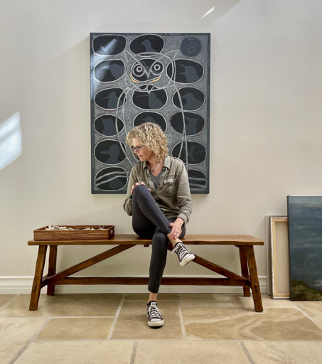 Elizabeth Shull sitting on a becnh in front of her painting
